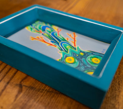 Formation in its handmade, hand-painted teal frame, lying on a wooden table.