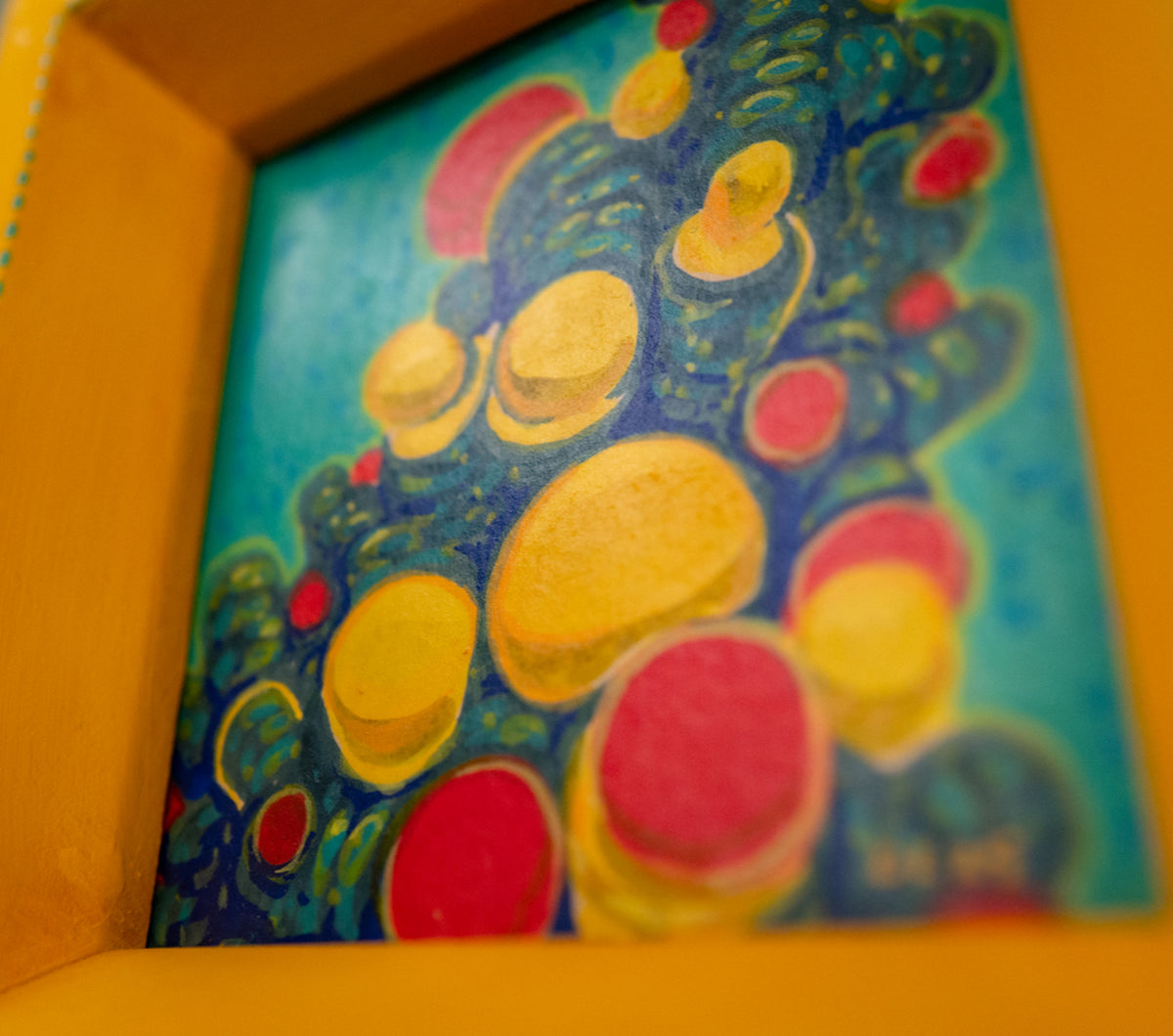 Angled close-up of Reconnecting in its yellow frame, showing the yellow and red bubbles on teal and the painted teal dots along the frame edge.