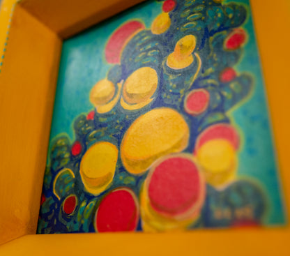 Angled close-up of Reconnecting in its yellow frame, showing the yellow and red bubbles on teal and the painted teal dots along the frame edge.
