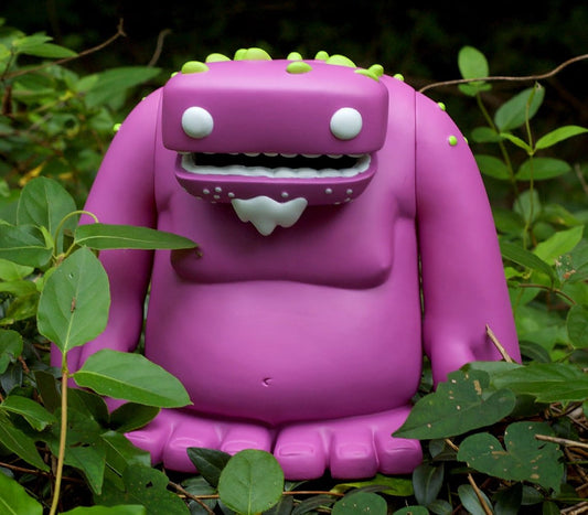 Zog vinyl toy: a purple monster with a toothy grin and green spots, standing among green leaves.
